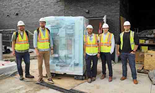 Five people in bright yellow construction vests outside of a brick building